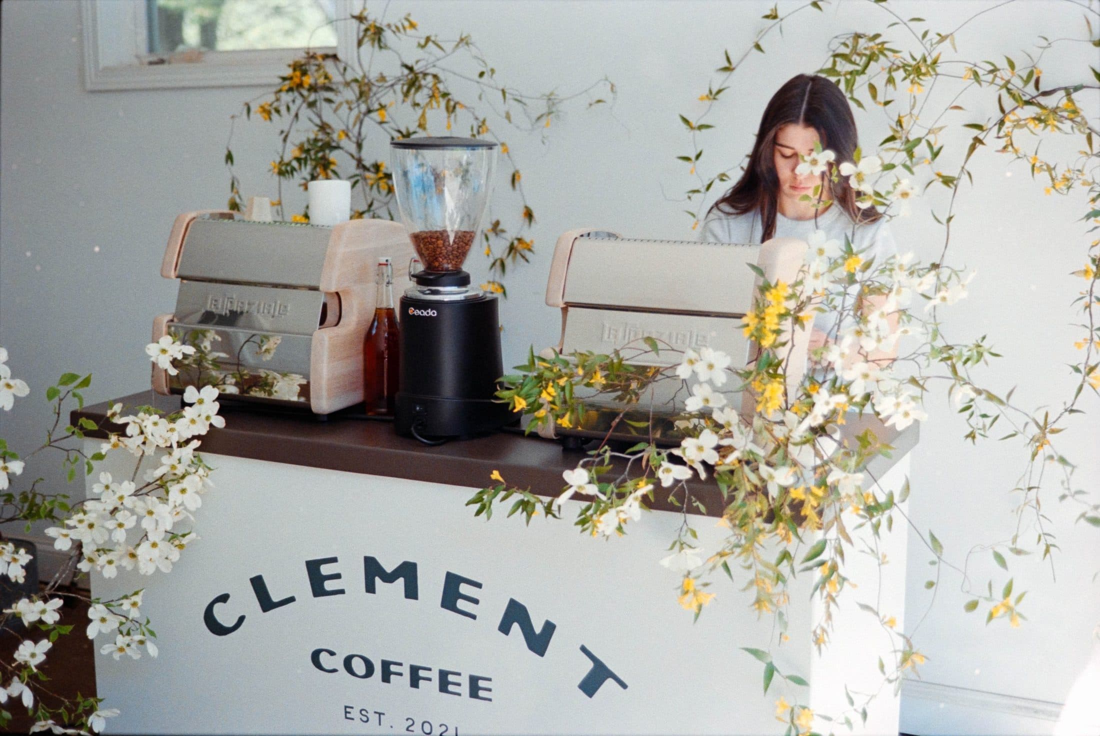 Clement Coffee mobile coffee cart with florals and a barista serving lattes at an event